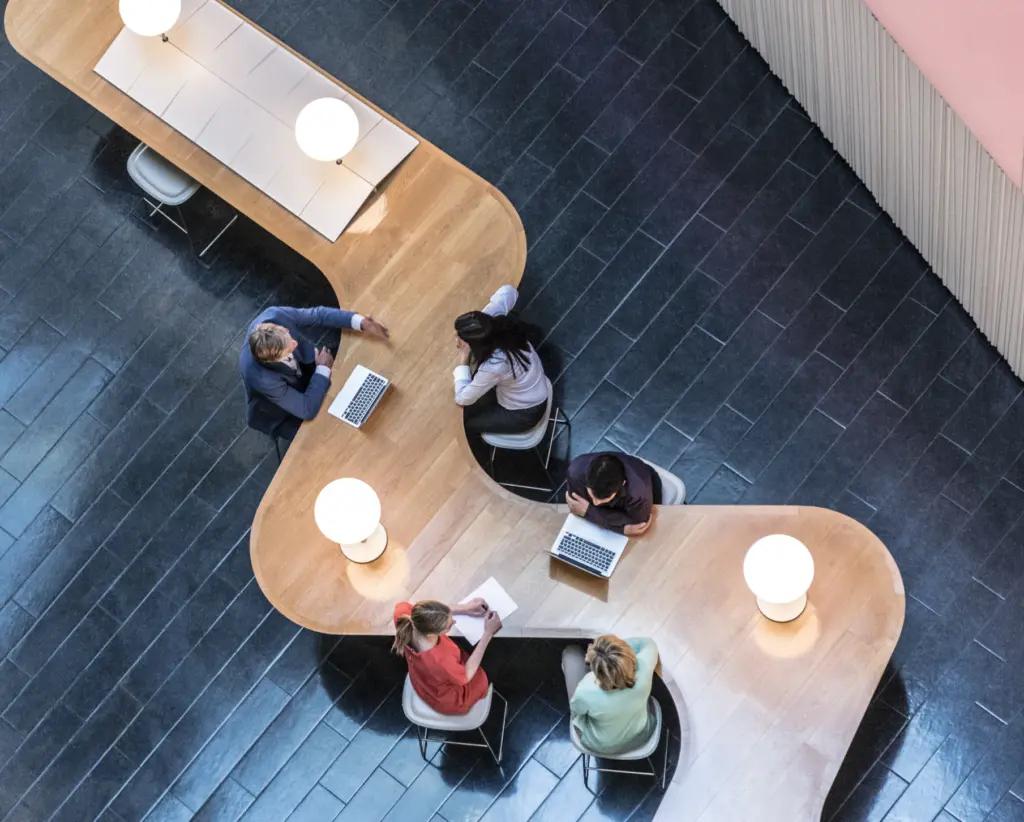 Aerial view of five people sitting at a curved wooden table talking to each other in groups